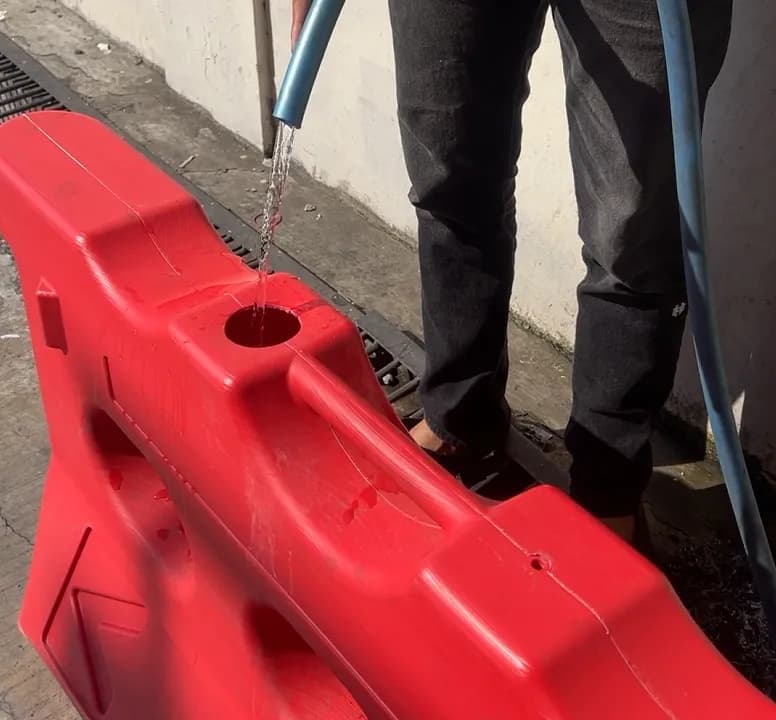 Foto detail road barrier HDPE Karpinus ketika diisi air melalui lubang bagian atas. Tampilkan selang, penutup lubang, dan bagian badan barrier dengan sudut kamera dekat